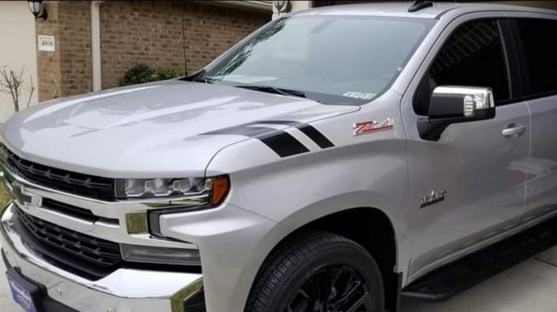 A silver truck with black stripes on the hood.